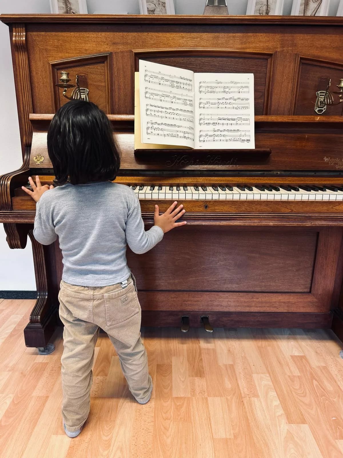 Young child standing at an upright piano with a music book open above the keys