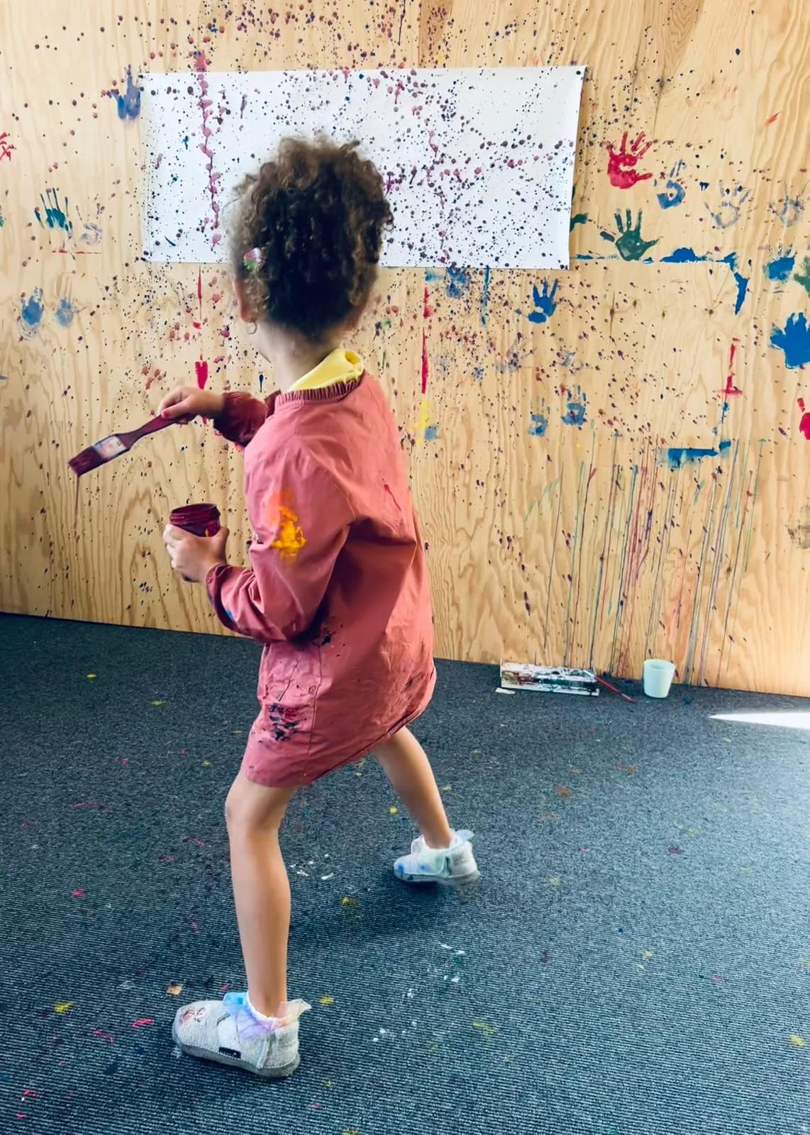 Child painting splatter-style on a wooden wall in the studio