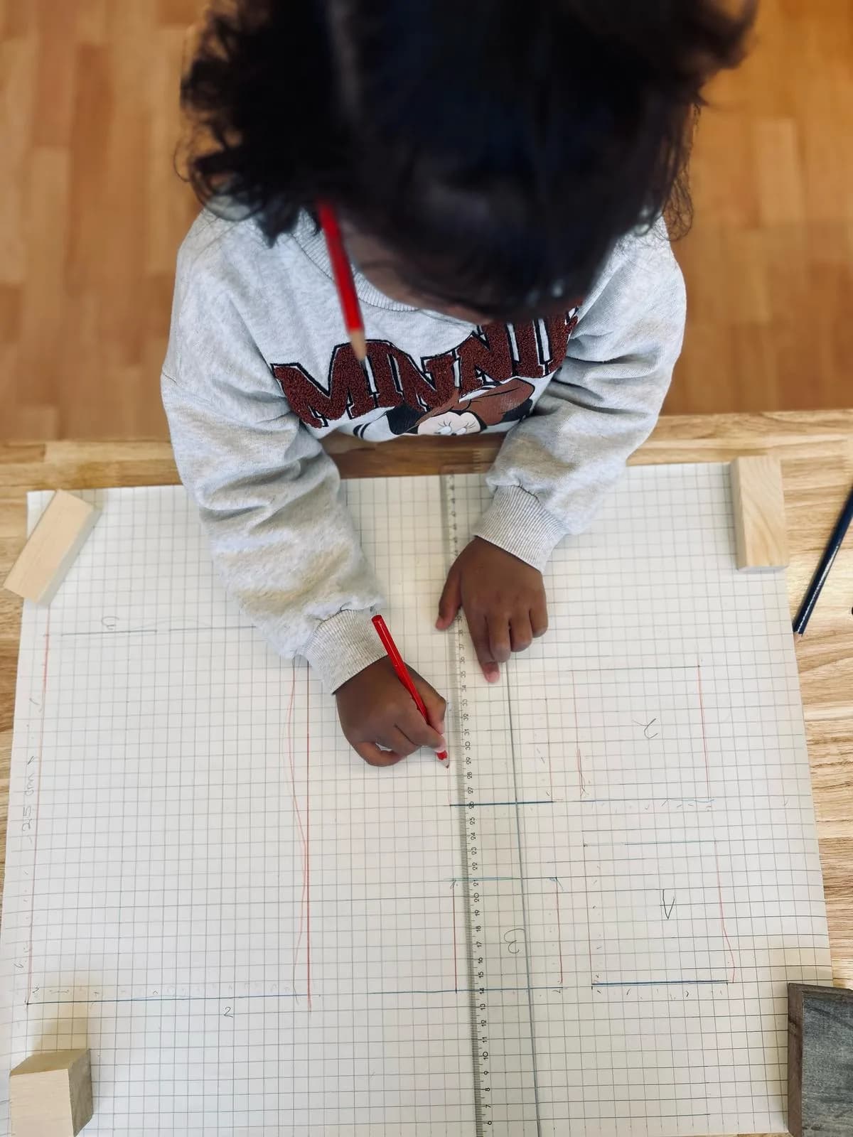 Child planning a woodworking project on grid paper with a ruler