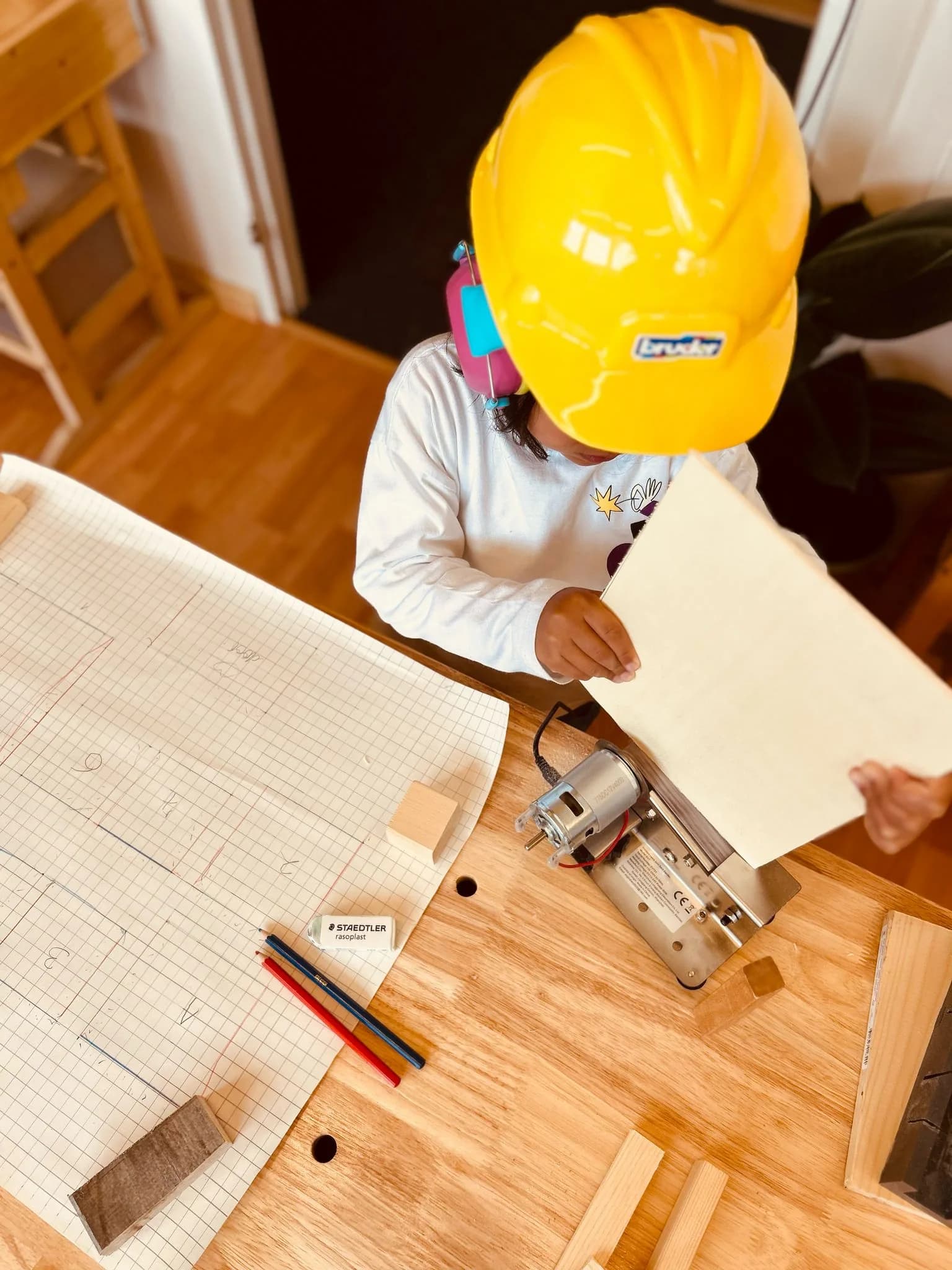 Child wearing a hard hat while reading a woodworking blueprint