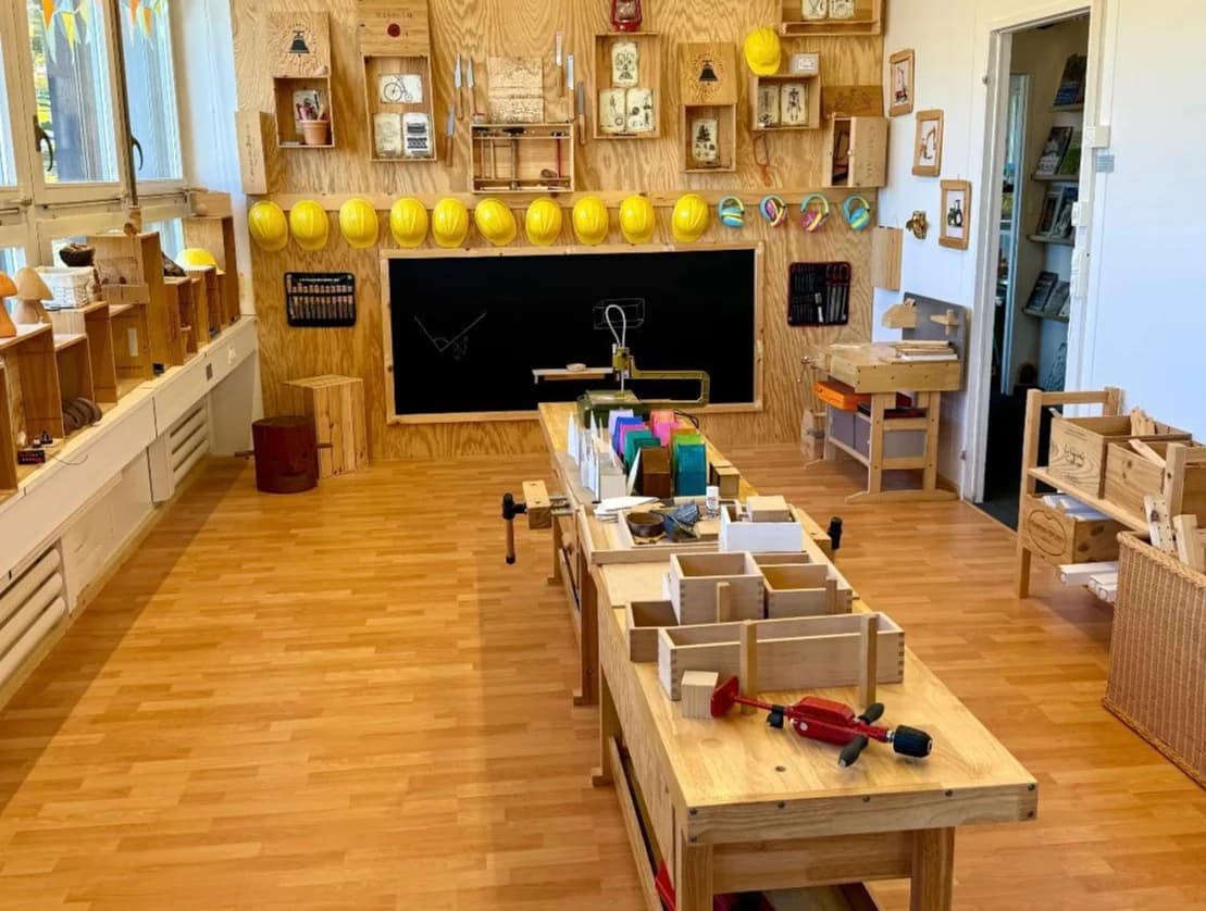 Bright woodworking room with workbenches, hard hats and a central blackboard
