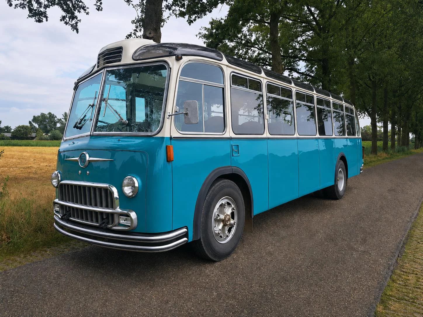 Der türkisfarbene Vintage-Schulbus des Montessori Traveling Classroom auf einer von Bäumen gesäumten Landstrasse